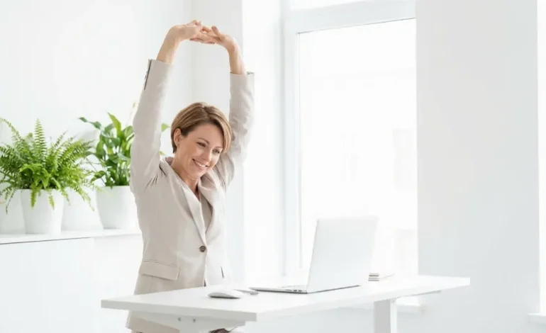 Zaposlena ženska se preteguje ob stoječi mizi v svetli pisarni